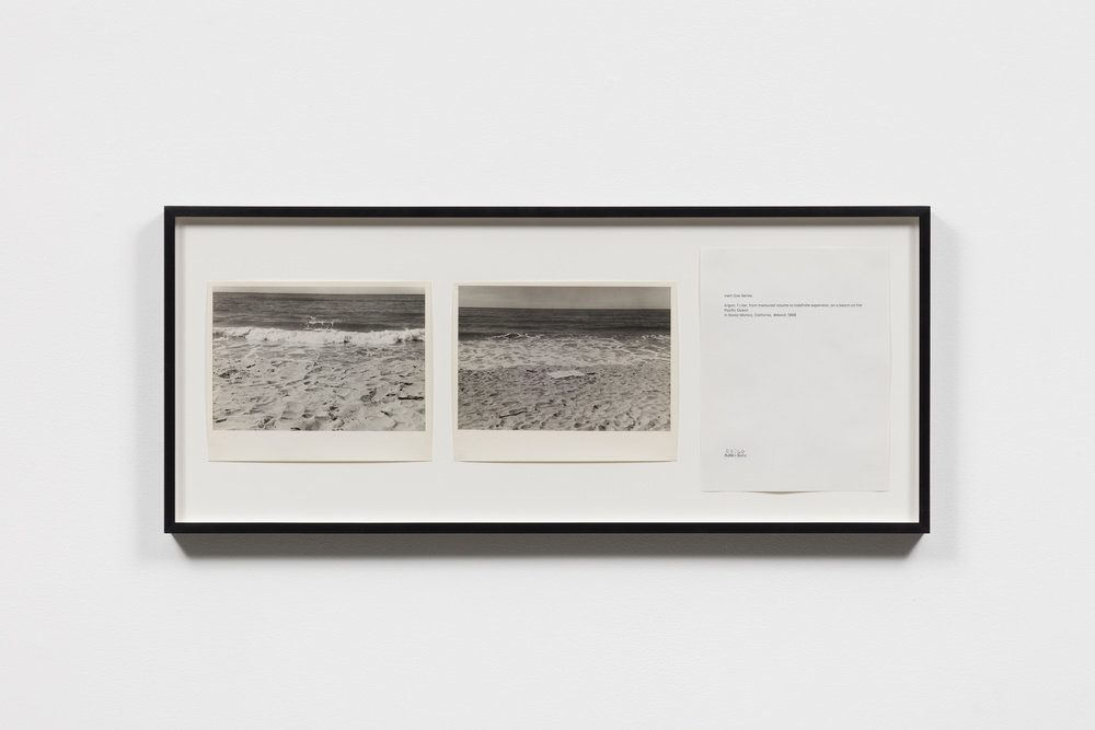 Two black and white photographs of the beach beside a white piece of paper with text, all hung in a black frame, by Robert Barry.